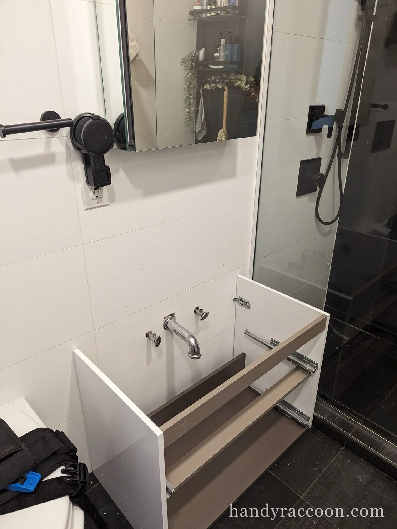 Vanity carcass with drawers pulled, chrome wall spout and shutoff valves during install in a bath.