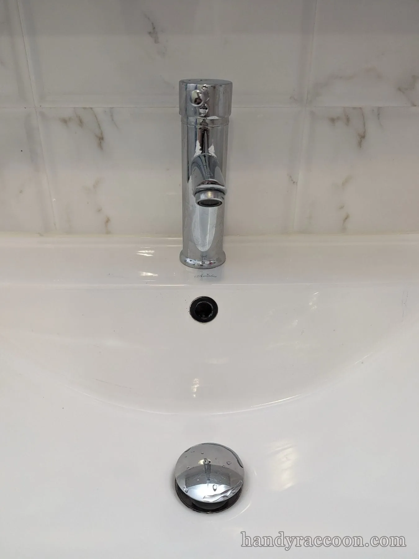 Chrome single-handle faucet mounted on a white ceramic basin against veined tile backsplash.