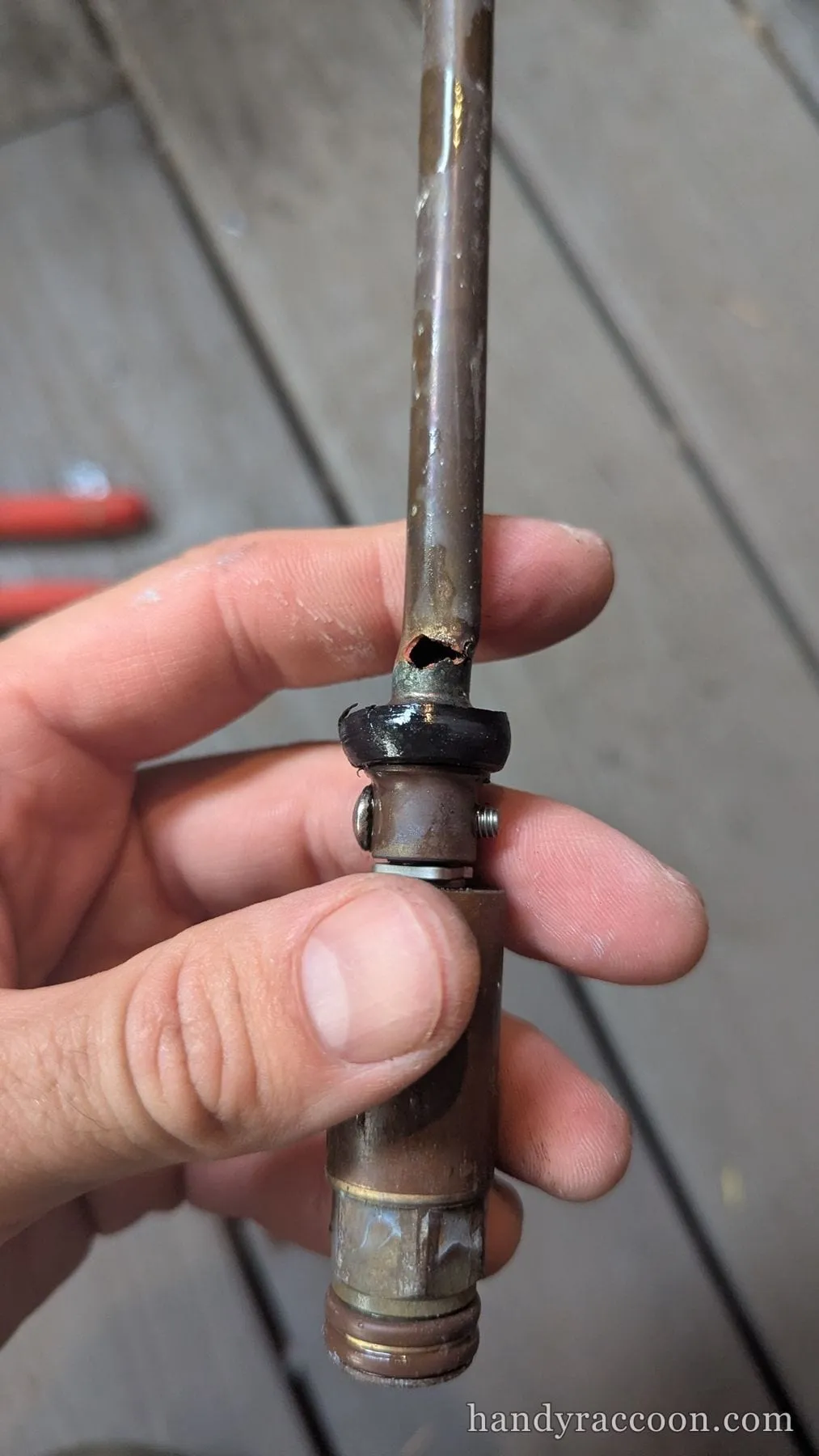 Hand holding a removed frost-free sillcock stem with a visible hole rusted through the brass tube.